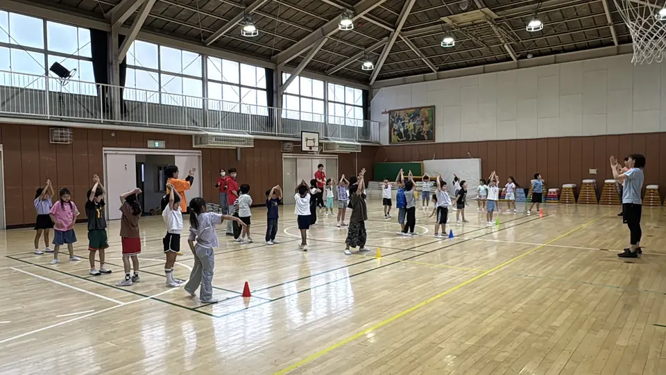 体育館で講師が児童全体へ動きを伝えている様子