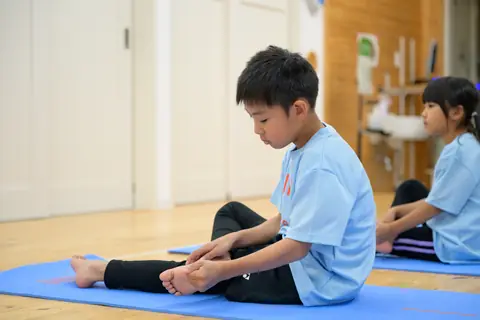 マットに座り、自分の足に触れて身体の感覚を確かめる子ども